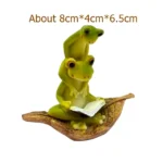 Frog couple seesaw figurine from behind, showing their tails and the seesaw mechanism, on soil.