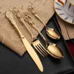 Gold flatware set with spoon, fork, and steak knife on a white tablecloth