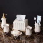 White porcelain rinsing cup with gold trim, placed beside a toothbrush holder in a bathroom.