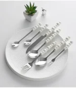 Stainless steel flatware set with ceramic pearl handles on wooden table
