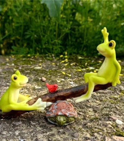 Fairy garden frog couple on a wooden seesaw in a miniature garden setting