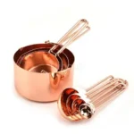 Set of stainless steel measuring cups with copper and rose gold finishes on wooden stand