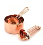 Set of stainless steel measuring cups with copper and rose gold finishes on wooden stand