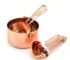 Set of stainless steel measuring cups with copper and rose gold finishes on wooden stand