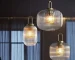Japanese style glass pendant light with clear glass shade and black cord, hanging over a wooden dining table.