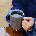 Double wall titanium mug with lid and tea strainer on a wooden table