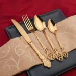 24-piece stainless steel cutlery set with gold handles displayed on a wooden table