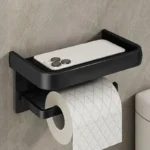 Aluminum toilet paper holder with shelf, holding a roll and small plant, angled from above.