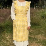 Woman wearing a cotton apron for baking with fresh plaid pattern and ruffled edges in a rustic kitchen