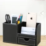 Leather PU pen holder storage box on a wooden desk with pens and remote controls inside.