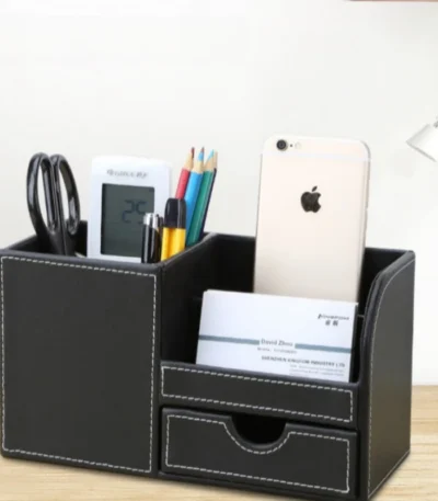 Leather PU pen holder storage box on a wooden desk with pens and remote controls inside.
