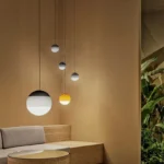 Gray glass pendant lamp with a metallic stem, shown in a contemporary living space.