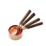 Set of stainless steel measuring cups with copper and rose gold finishes on wooden stand