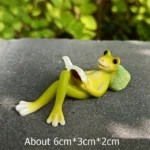 Cute frog couple figurine on seesaw, detailed with glossy paint, placed on a wooden slice.