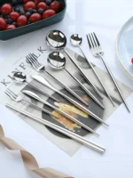 Elegant stainless steel flatware set with forks, spoons, and knives arranged on a wooden table