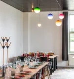 Pink glass pendant lamp hanging low over a round table with chairs in a cafe setting.