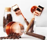 Set of stainless steel measuring cups with copper and rose gold finishes on wooden stand