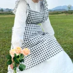 Woman wearing a cotton apron for baking with fresh plaid pattern and ruffled edges in a rustic kitchen