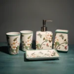 Bathroom decor set: ceramic toothbrush holder, cup, and lotion bottle, on white cabinet.