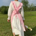 Woman wearing a cotton apron for baking with fresh plaid pattern and ruffled edges in a rustic kitchen
