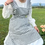 Woman wearing a cotton apron for baking with fresh plaid pattern and ruffled edges in a rustic kitchen