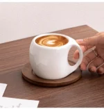 Elegant ceramic coffee mug set with saucer on wooden table, featuring oat-colored cups