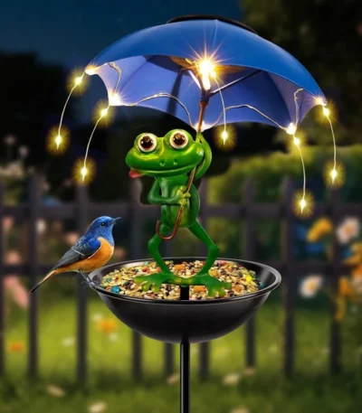Solar frog garden light with umbrella illuminating a flower bed at dusk