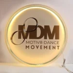 Round illuminated logo sign with a sleek black acrylic base, shown on a shelf with office books.
