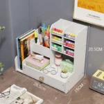 Multi-grid storage pen holder on a shelf, surrounded by books and a small plant.
