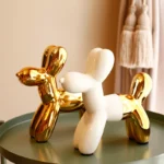 Gold ceramic balloon dog statue on a white shelf against a beige wall.