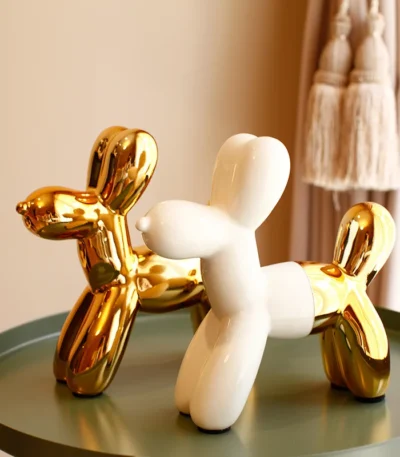 Gold ceramic balloon dog statue on a white shelf against a beige wall.