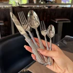 Elegant stainless steel flatware set with mirror finish arranged on a wooden table