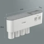 White automatic toothpaste dispenser with toothbrush holder, cups, and rack set on a modern bathroom counter.