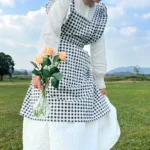 Woman wearing a cotton apron for baking with fresh plaid pattern and ruffled edges in a rustic kitchen