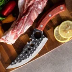Goldoma scimitar chef knife slicing through raw meat on a cutting board