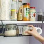 Metal under shelf basket hanging from a kitchen shelf, holding spices and small jars
