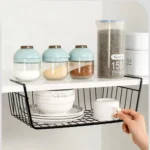 Metal under shelf basket hanging from a kitchen shelf, holding spices and small jars