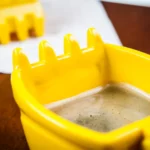 Excavator mug with spoon on a wooden table, ceramic bucket-shaped mug with a metal shovel spoon