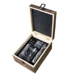 Old fashioned glass set with whiskey tumblers, ice stones, and wooden gift box on a rustic table