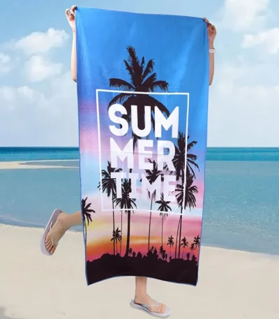 Vibrant summer travel beach towel with palm tree print, laid on sandy shore