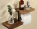 Wooden toilet paper holder mounted on a white bathroom wall with a roll of tissue hanging down.