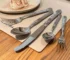 Elegant stainless steel cutlery set with steak knife, fork, spoon, and fruit fork on a wooden table