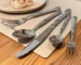 Elegant stainless steel cutlery set with steak knife, fork, spoon, and fruit fork on a wooden table