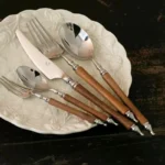 Elegant stainless steel dinnerware set with wooden handles on a rustic table