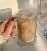 Set of transparent glass coffee mugs with lids and straws on a wooden table