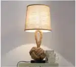 Vintage table lamp with hemp rope and iron base, emitting warm light on a bedside table
