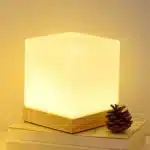 Modern table lamp with iron body and wood base illuminating a cozy bedroom