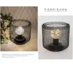 Decorative bird cage lamp with warm LED light, iron frame, and silk screen details on a bedside table