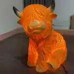 Whimsical cow table lamp with highland cattle design, casting a warm glow on a bedside table