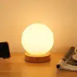Modern table lamp with iron body and wood base illuminating a cozy bedroom